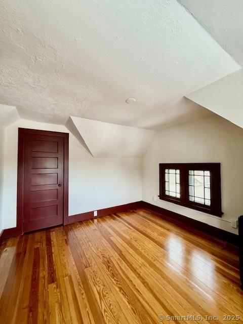 additional living space with lofted ceiling, a textured ceiling, baseboards, and hardwood / wood-style flooring