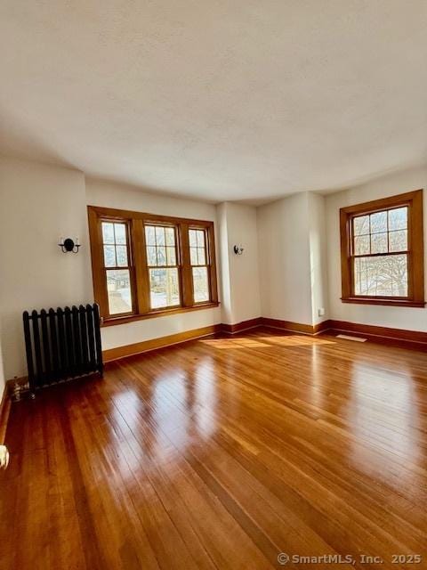 empty room with visible vents, baseboards, hardwood / wood-style floors, and radiator heating unit