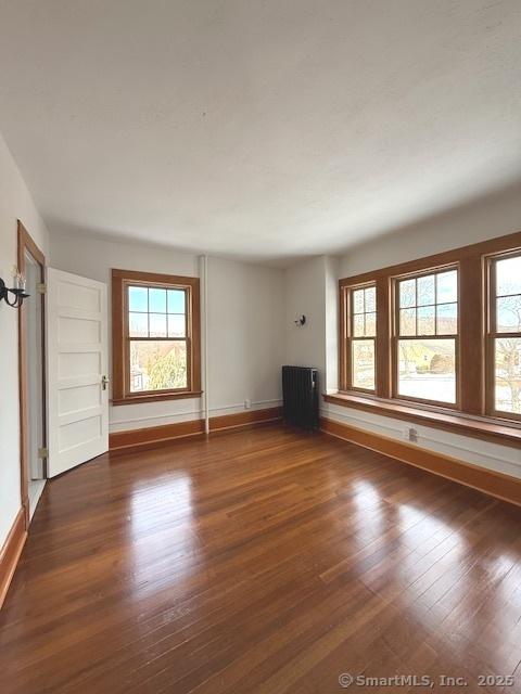 unfurnished living room featuring radiator heating unit, dark wood finished floors, and a healthy amount of sunlight