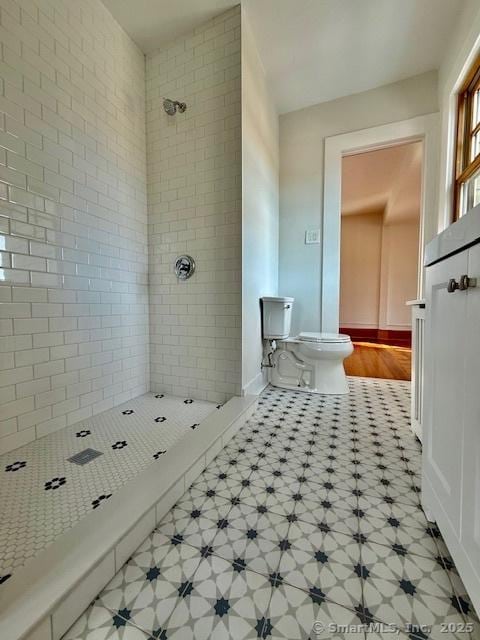 bathroom featuring toilet, baseboards, tiled shower, and tile patterned floors