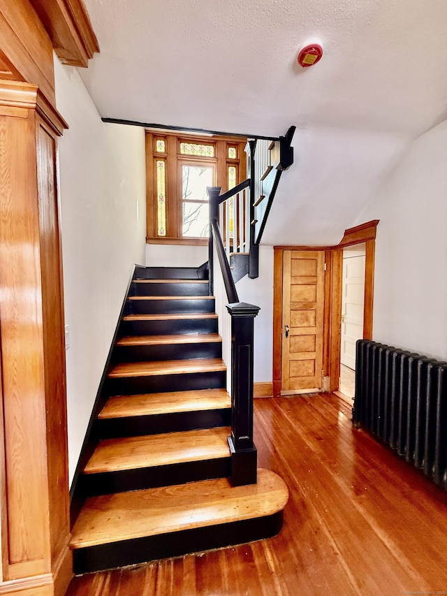 staircase with radiator, vaulted ceiling, baseboards, and wood finished floors