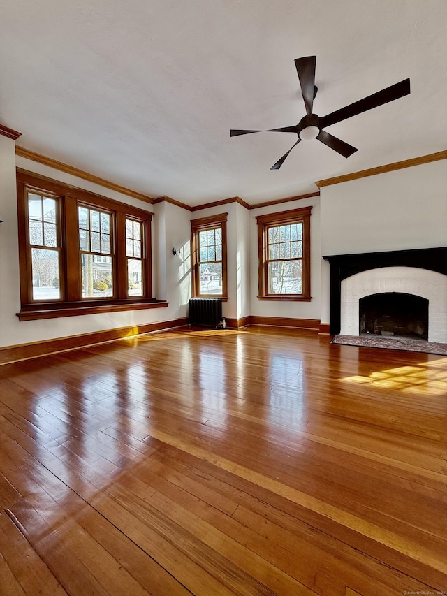 unfurnished living room featuring a fireplace with flush hearth, baseboards, radiator heating unit, wood-type flooring, and crown molding