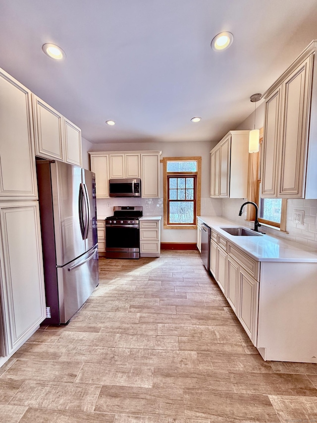 kitchen featuring stainless steel appliances, tasteful backsplash, light countertops, light wood-style flooring, and a sink