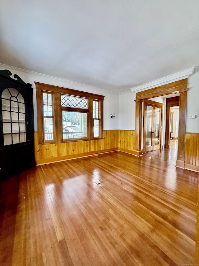 unfurnished living room featuring ornamental molding, wood finished floors, and wainscoting