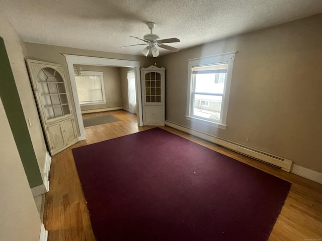 spare room with a textured ceiling, a baseboard radiator, a baseboard heating unit, baseboards, and light wood-style floors