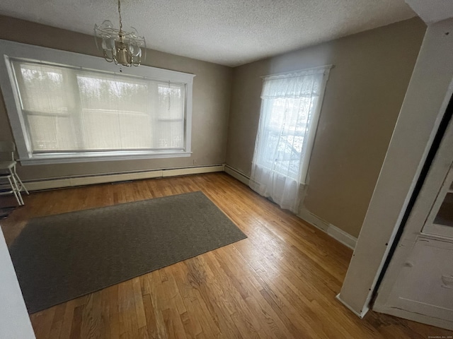 unfurnished dining area featuring a chandelier, a baseboard radiator, light wood-style flooring, and a textured ceiling