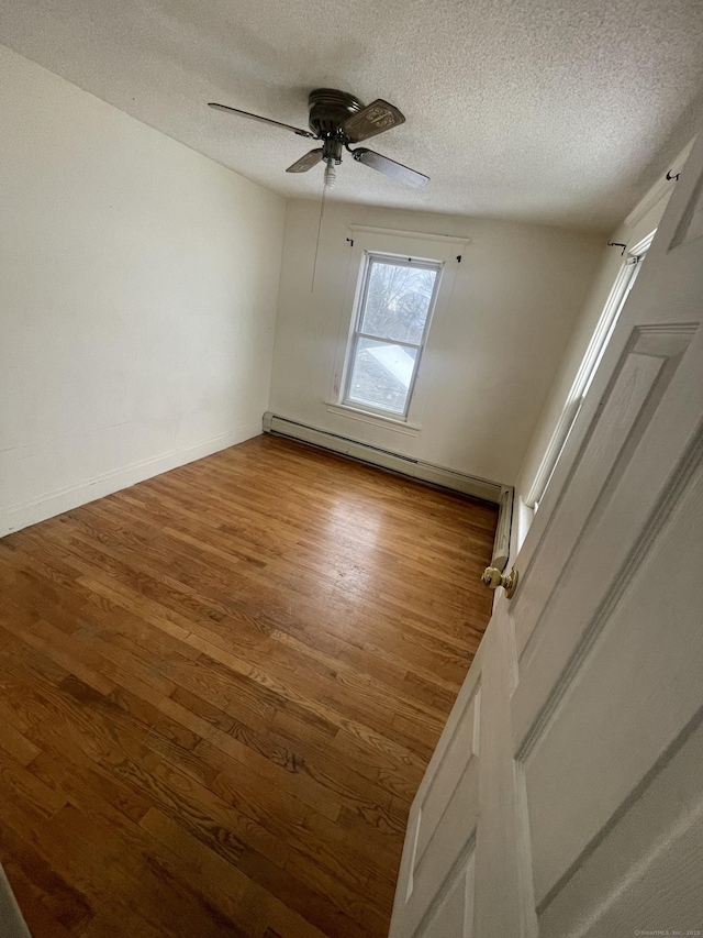 spare room with a baseboard heating unit, a ceiling fan, a textured ceiling, wood finished floors, and baseboards