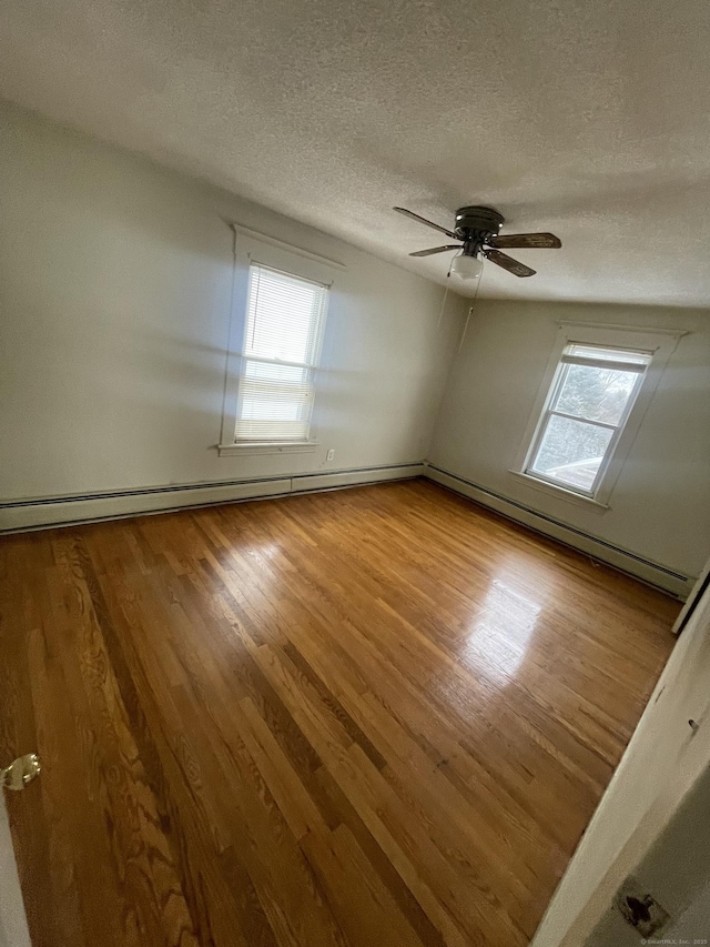 spare room with a ceiling fan, a wealth of natural light, a textured ceiling, and wood finished floors