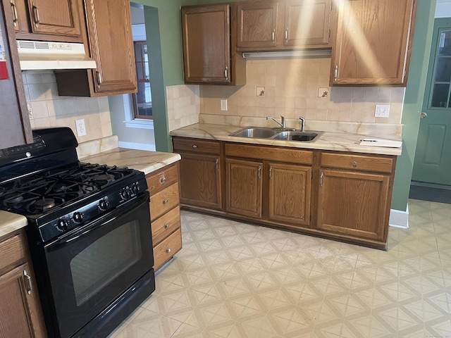 kitchen featuring under cabinet range hood, a sink, light countertops, light floors, and black gas range oven