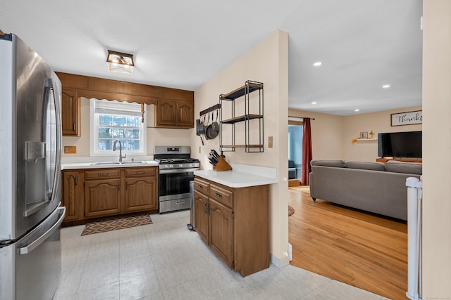 kitchen featuring brown cabinetry, appliances with stainless steel finishes, open floor plan, light countertops, and a sink