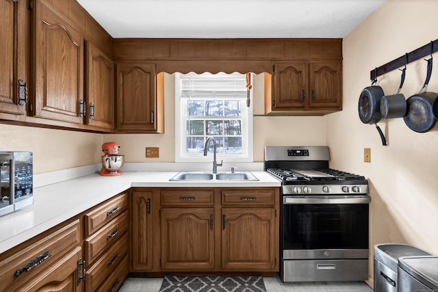 kitchen with brown cabinets, light countertops, stainless steel range with gas stovetop, and a sink