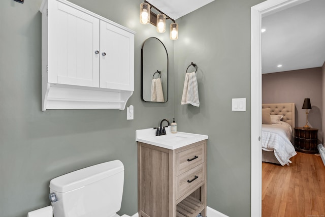 bathroom featuring toilet, ensuite bathroom, vanity, wood finished floors, and baseboards