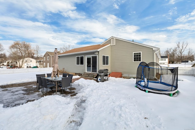 snow covered property with a trampoline, entry steps, and fence