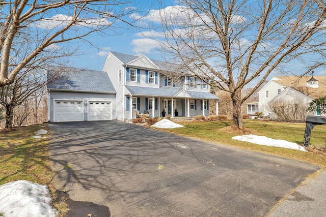 view of front facade featuring roof with shingles, covered porch, an attached garage, driveway, and a front lawn