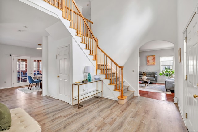 foyer entrance featuring stairs, arched walkways, wood finished floors, and a towering ceiling