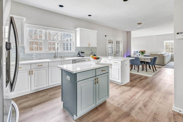 kitchen with stainless steel appliances, a kitchen island, a sink, light wood-style floors, and white cabinets