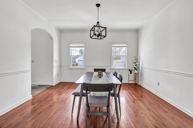 dining room featuring arched walkways, ornamental molding, hardwood / wood-style flooring, and baseboards