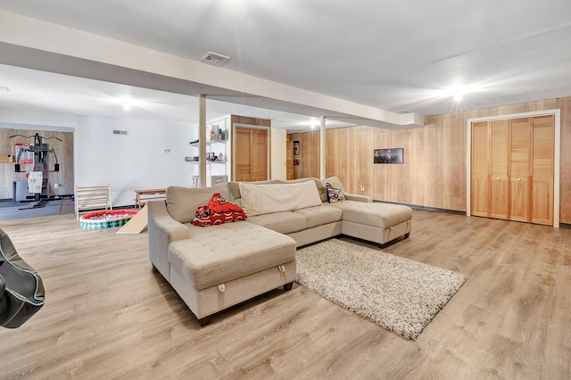 living area with light wood-type flooring, visible vents, and wood walls