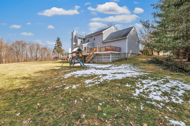 snow covered back of property with a yard, a chimney, and a wooden deck