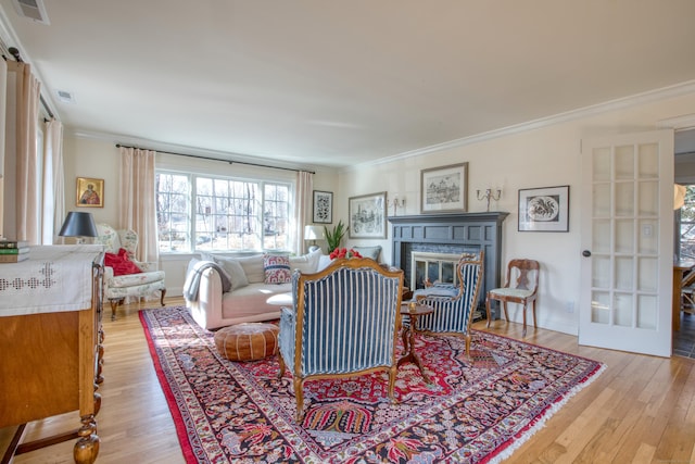 living room featuring ornamental molding, a glass covered fireplace, and visible vents