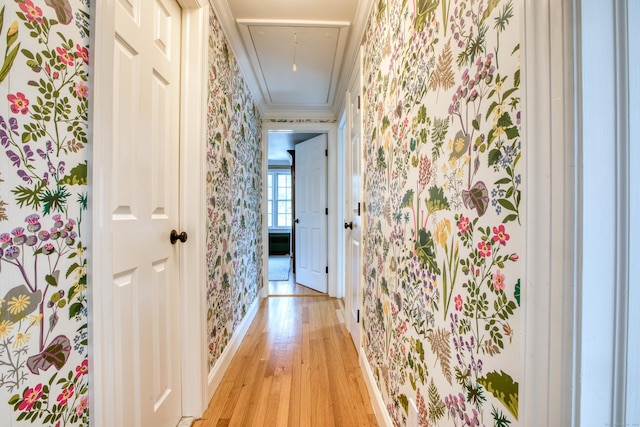 corridor featuring crown molding, light wood-type flooring, attic access, and wallpapered walls