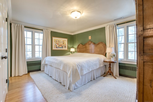 bedroom with radiator, light wood-type flooring, visible vents, and ornamental molding