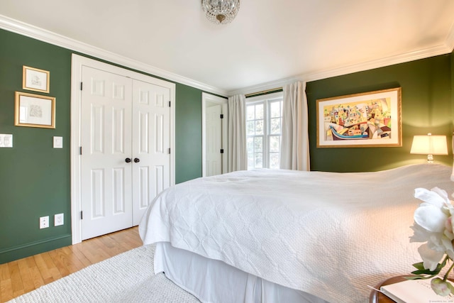 bedroom with a closet, baseboards, crown molding, and wood finished floors