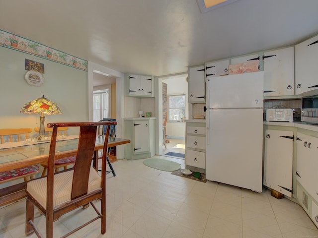 kitchen with tasteful backsplash, stainless steel microwave, freestanding refrigerator, light countertops, and white cabinetry