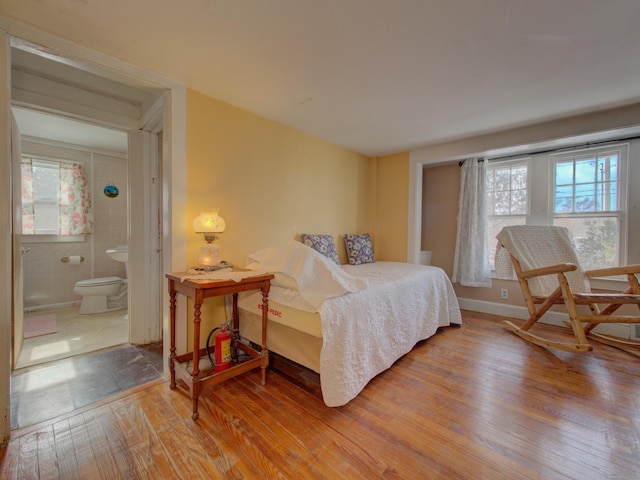 bedroom with ensuite bathroom, multiple windows, wood-type flooring, and baseboards