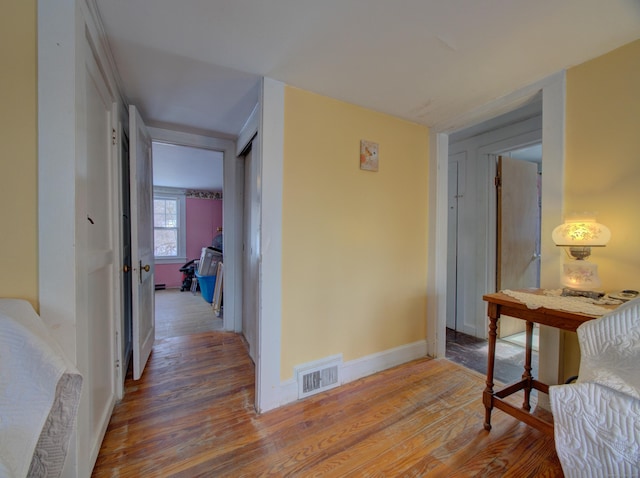 corridor featuring baseboards, visible vents, and wood finished floors