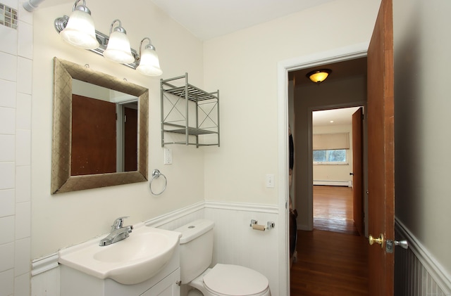 bathroom with baseboard heating, toilet, wainscoting, vanity, and wood finished floors