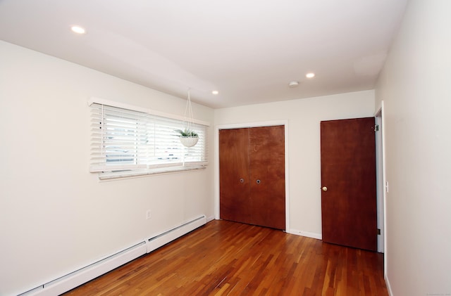 unfurnished bedroom with recessed lighting, a closet, baseboard heating, and wood finished floors