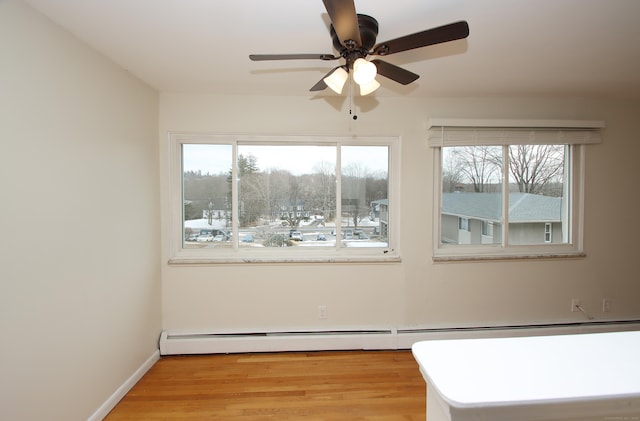 empty room with baseboard heating, light wood-type flooring, a ceiling fan, and baseboards