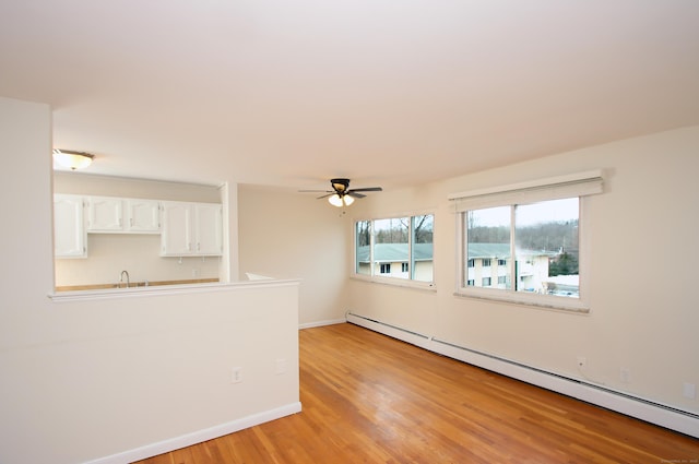 spare room featuring light wood-type flooring, baseboards, baseboard heating, and a ceiling fan