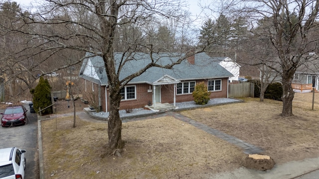 view of front of house featuring driveway, brick siding, a chimney, and fence