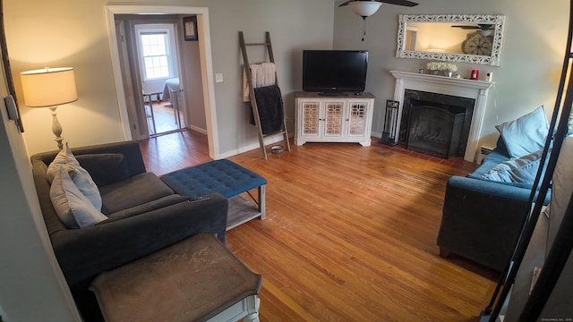 living area featuring a fireplace with flush hearth, ceiling fan, wood finished floors, and baseboards