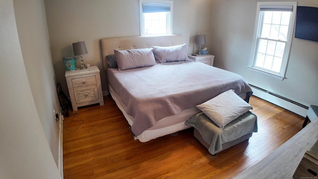 bedroom with a baseboard heating unit, multiple windows, and light wood-style flooring