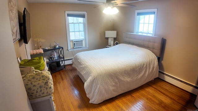 bedroom with a baseboard heating unit, cooling unit, multiple windows, and hardwood / wood-style floors