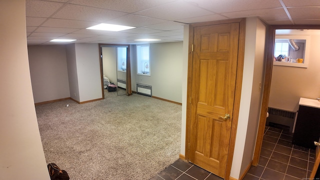 basement featuring dark colored carpet, radiator, a drop ceiling, and baseboards