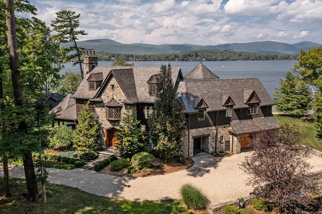 view of front of home with stone siding, dirt driveway, a chimney, and a water and mountain view