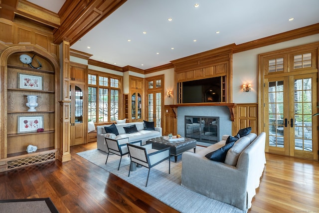 living area featuring ornamental molding, french doors, wood finished floors, and a glass covered fireplace