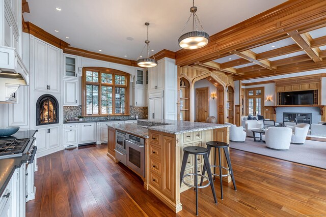 kitchen with arched walkways, appliances with stainless steel finishes, dark wood-type flooring, open floor plan, and glass insert cabinets