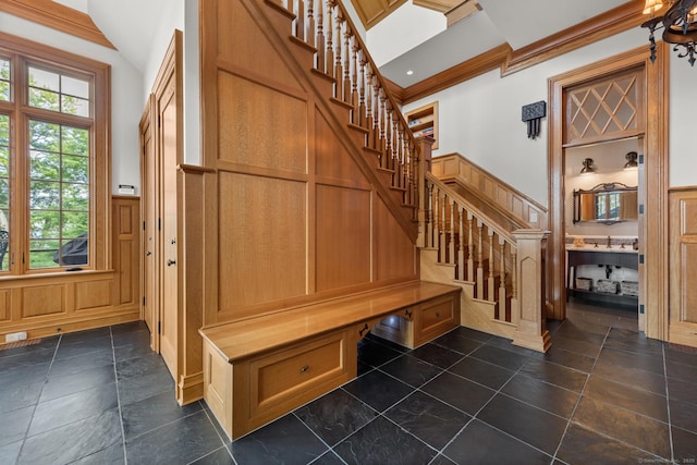 mudroom with lofted ceiling, a wainscoted wall, crown molding, and a decorative wall