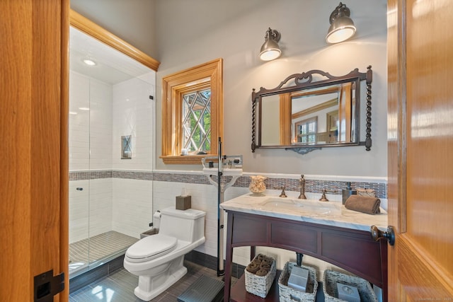 bathroom featuring a stall shower, wainscoting, toilet, vanity, and tile walls