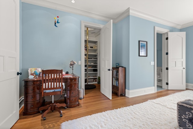 bedroom featuring a closet, a spacious closet, ornamental molding, wood finished floors, and baseboards