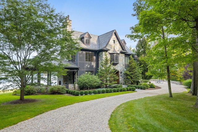 view of front of house with driveway, stone siding, and a front lawn