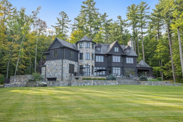 back of house featuring stone siding, a lawn, and a chimney