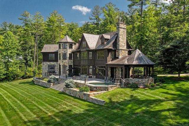 rear view of property with a patio area, an in ground hot tub, a lawn, and stone siding