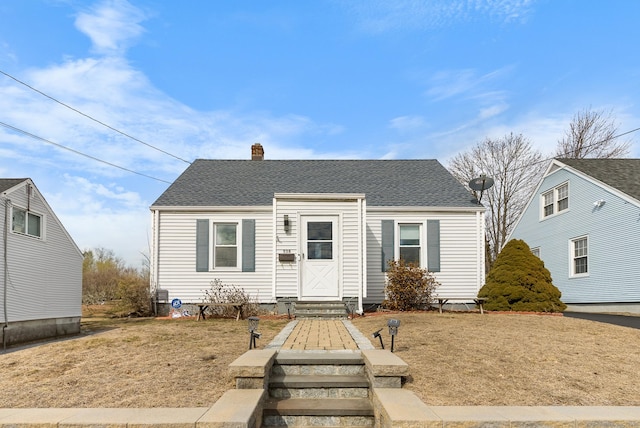 bungalow with entry steps, a front yard, a chimney, and roof with shingles