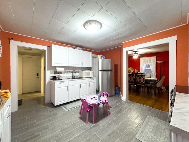 kitchen with light countertops, white microwave, freestanding refrigerator, white cabinets, and a sink